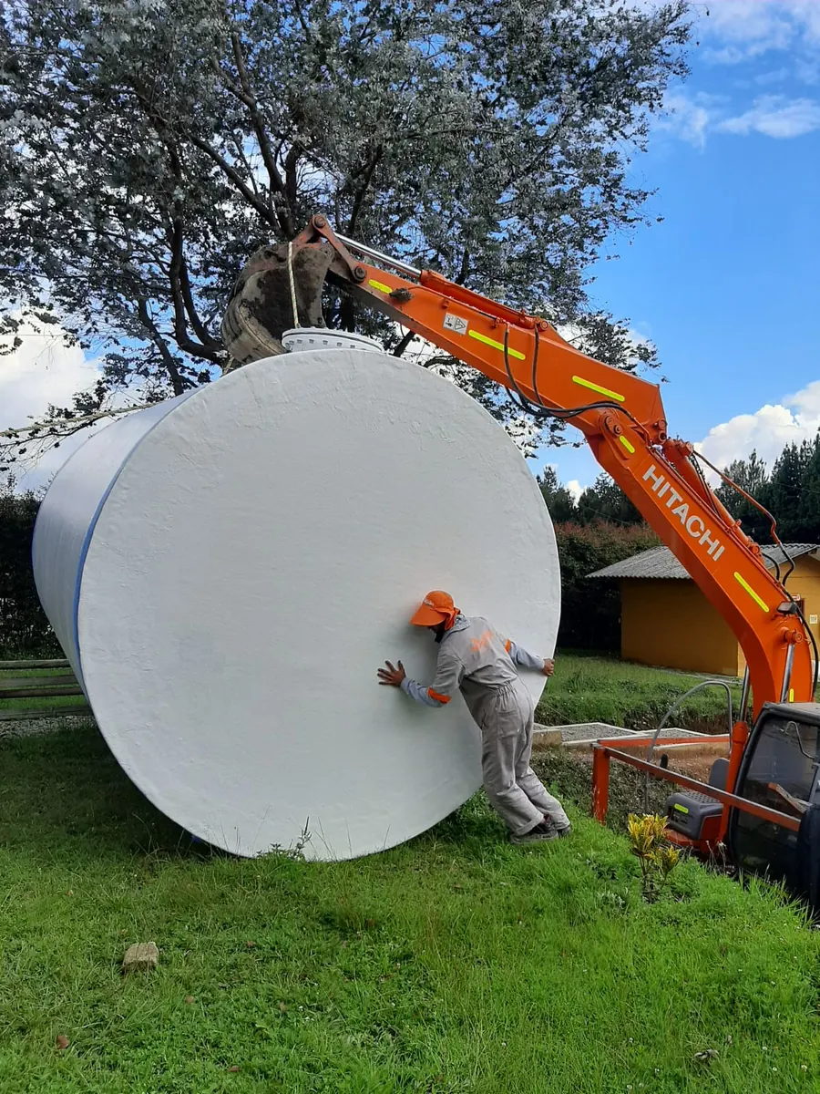 Operario de pie junto a un tanque vertical en fibra de vidrio que lo dobla en altura, dentro de la planta de Fibremos.